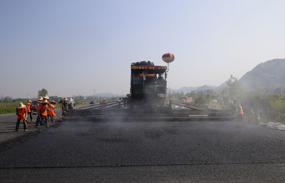 2019年8月，宜春經(jīng)開區(qū)S311路面攤鋪現(xiàn)場，工友們輔助路面兩側(cè)的分料、補窩等作業(yè)